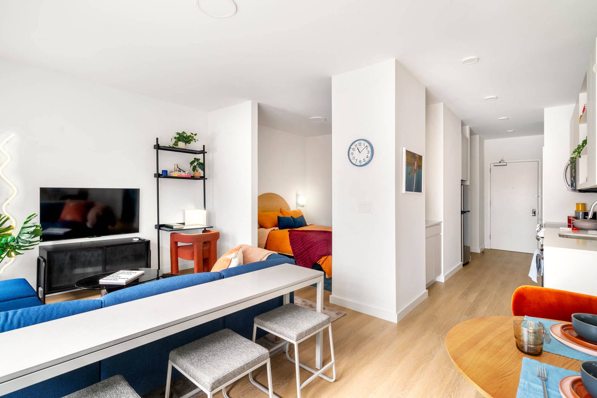a dining room with a table and chairs and a potted plant,,a living room with a blue couch and a kitchen,a living room with a couch and a table,