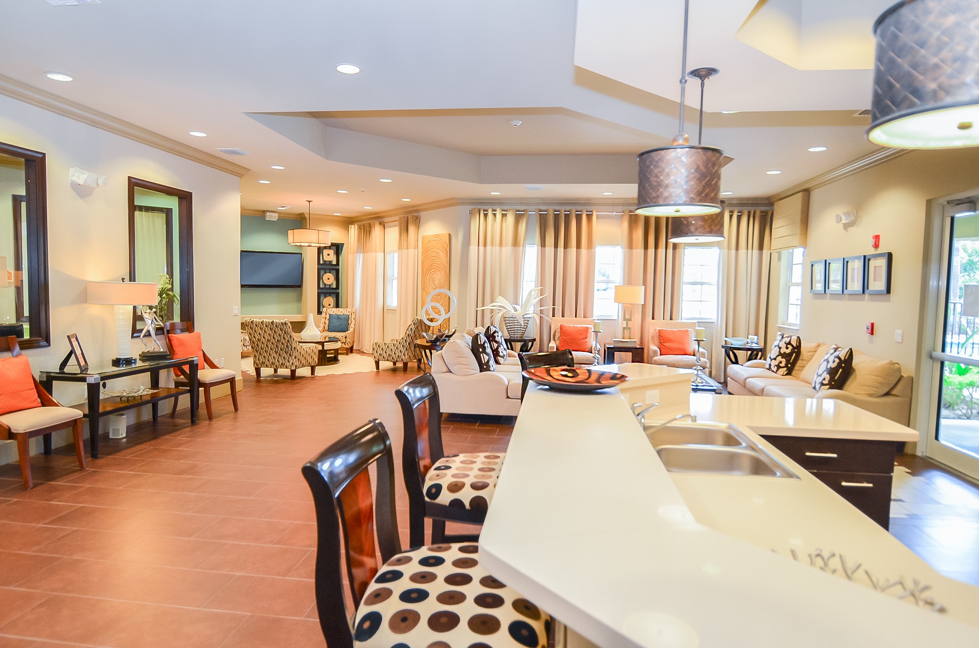 A modern kitchen with a long white island and brown chairs.