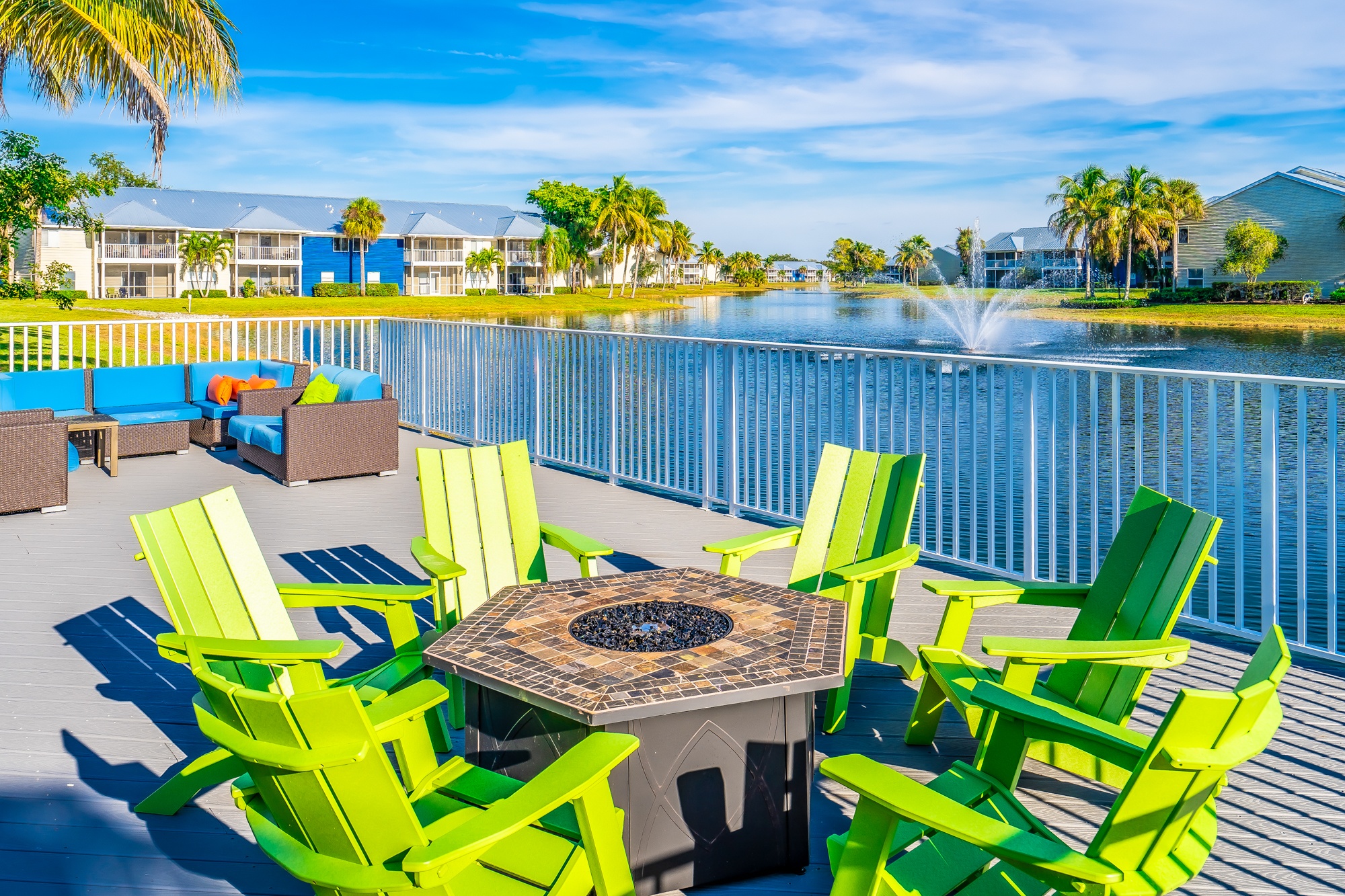 A table surrounded by green chairs is in the foreground of a sunny patio.