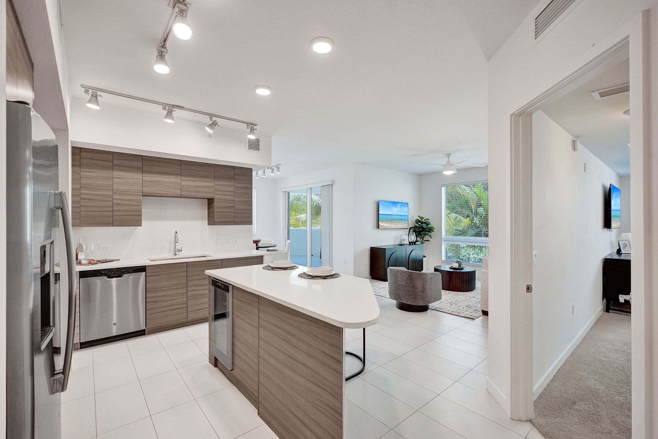 A modern kitchen with a refrigerator on the left and a dining area with a table and chairs in the background.