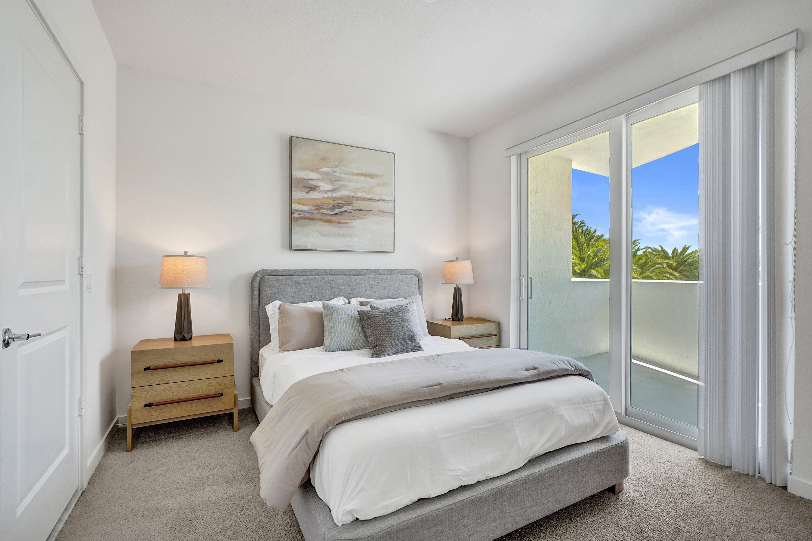 A bedroom with a large bed, two lamps, and a painting on the wall.