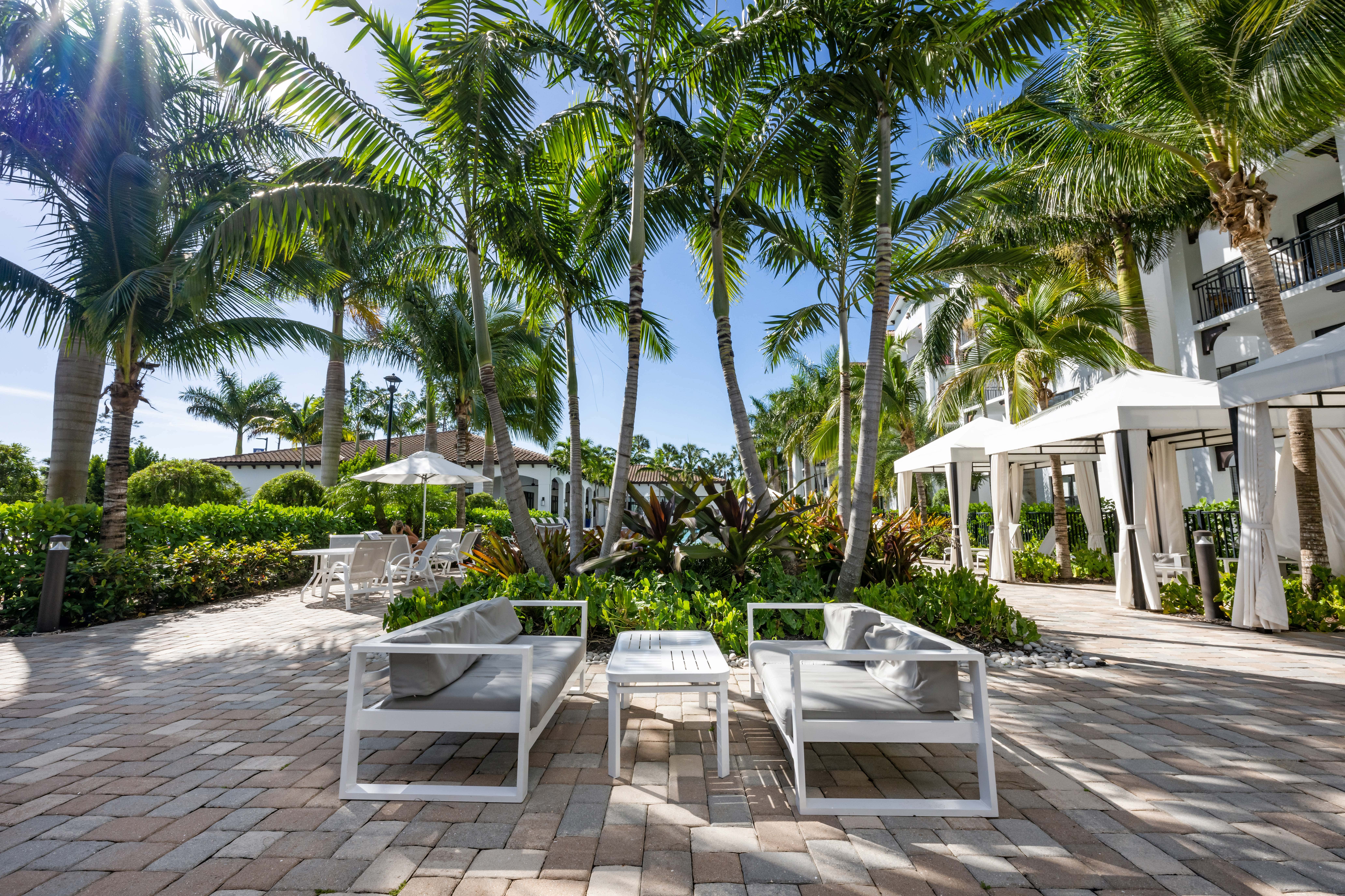 Two white lounge chairs are on a patio with palm trees in the background.