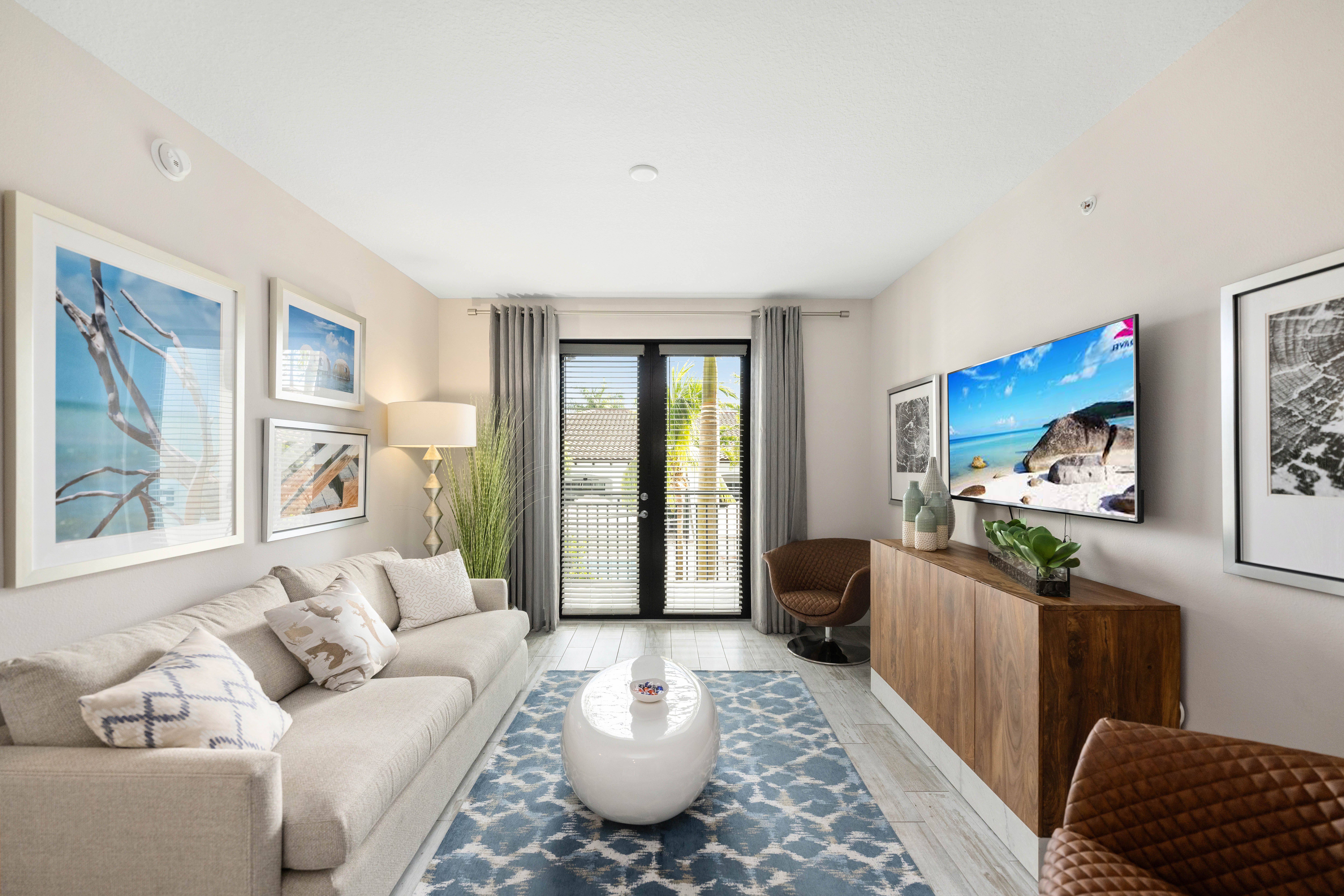 A modern living room with a white sofa, a TV, and a large window with curtains.