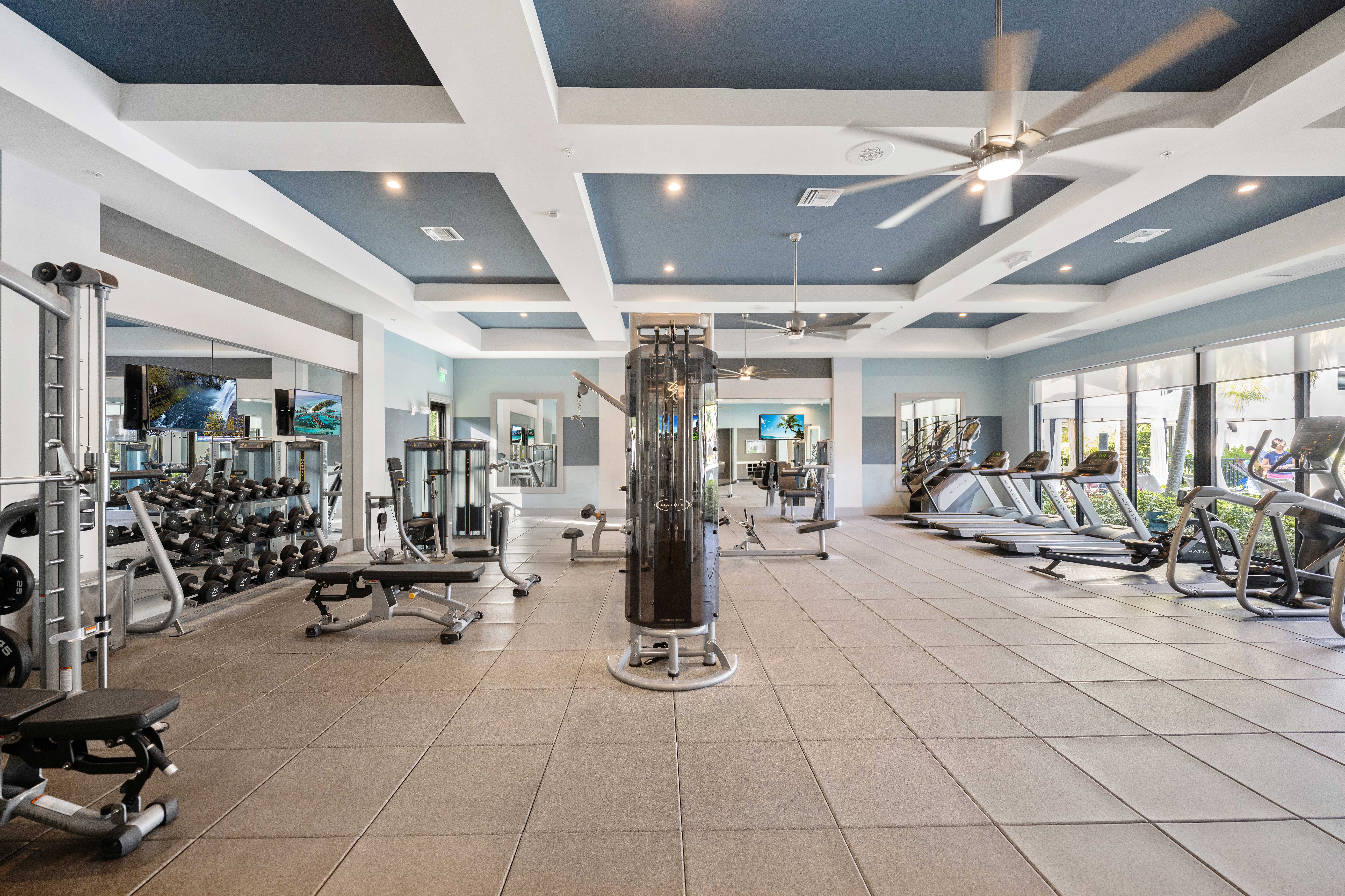 A spacious gym with a variety of equipment and a fan on the ceiling.