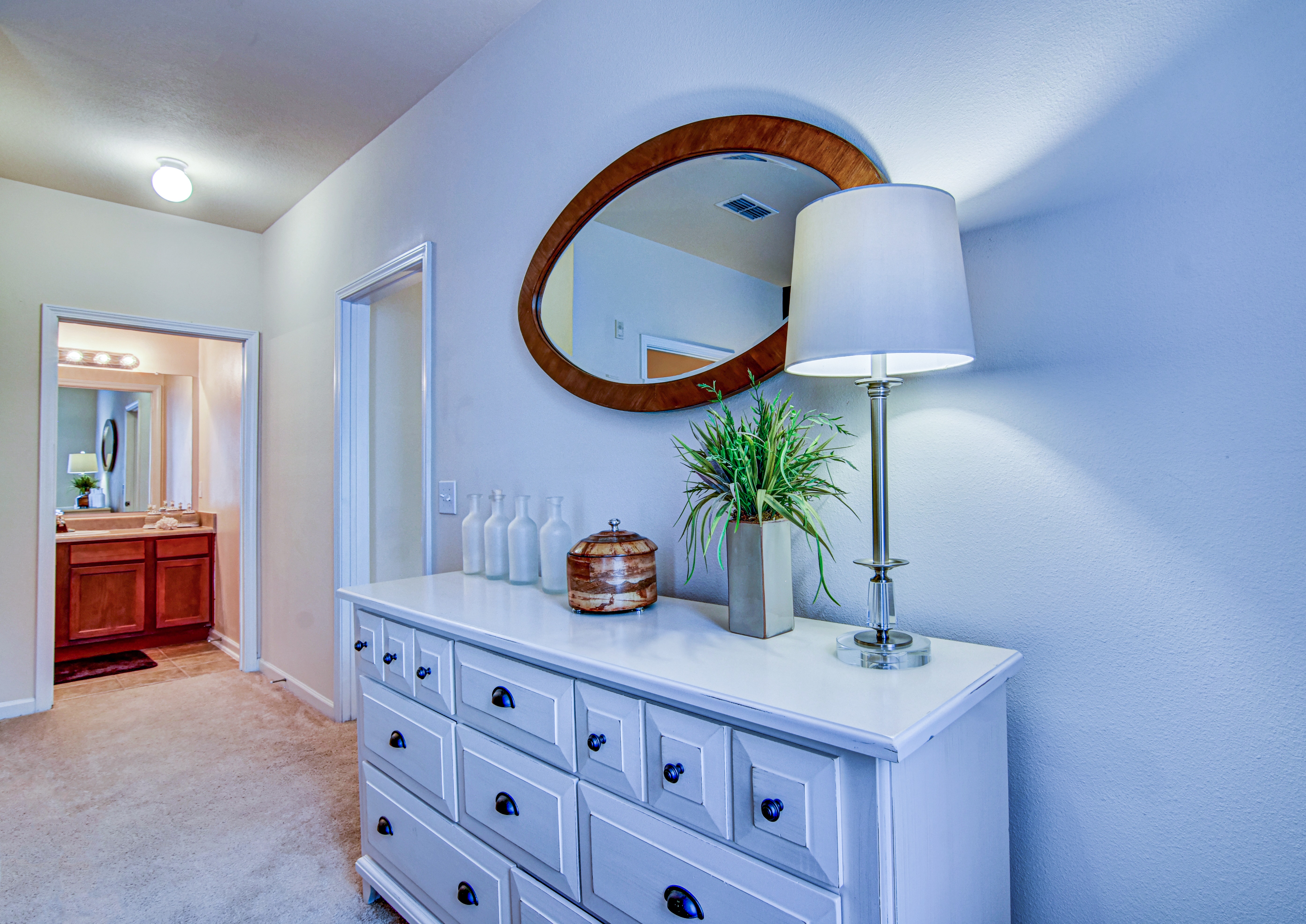 A white dresser with a round mirror above it and a potted plant on top.