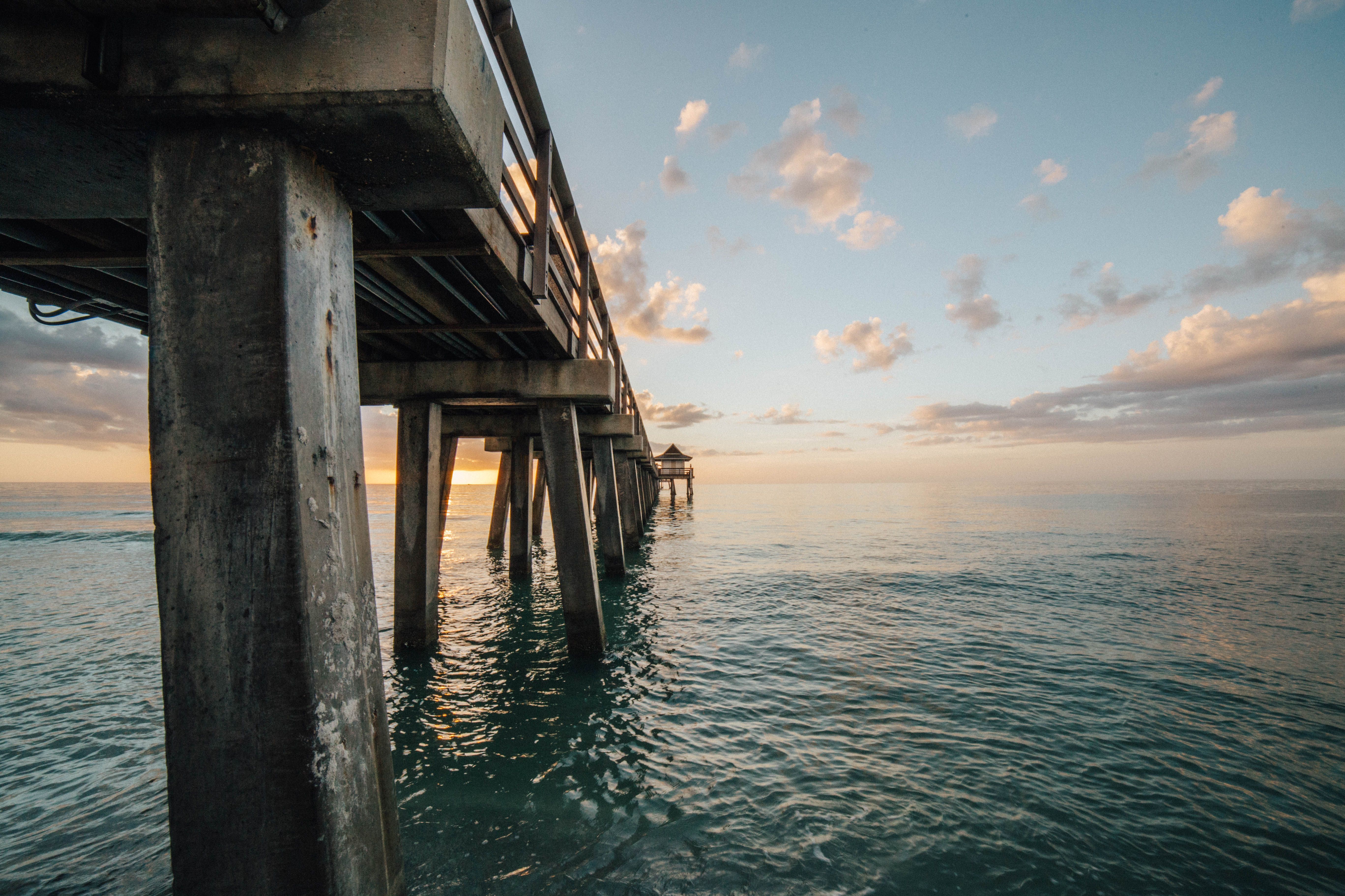 A long wooden pier extends into a calm body of water under a partly cloudy sky.