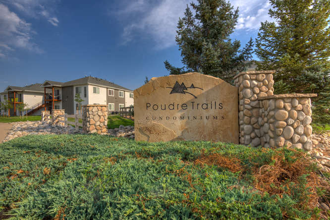 a stone sign that says pouce trails condominiums with a building in the background
