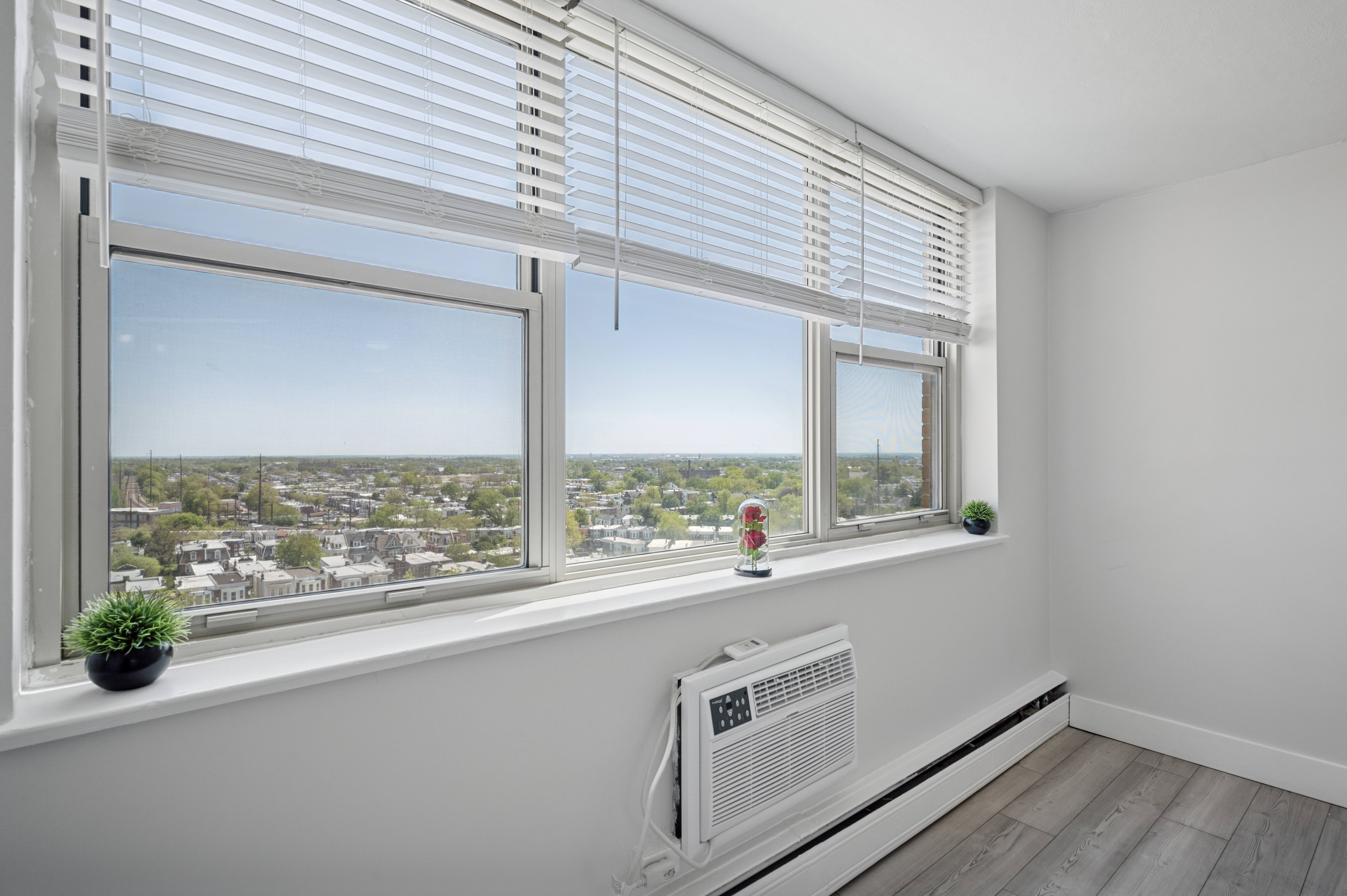 A room with a window overlooking a cityscape and a white radiator on the floor.
