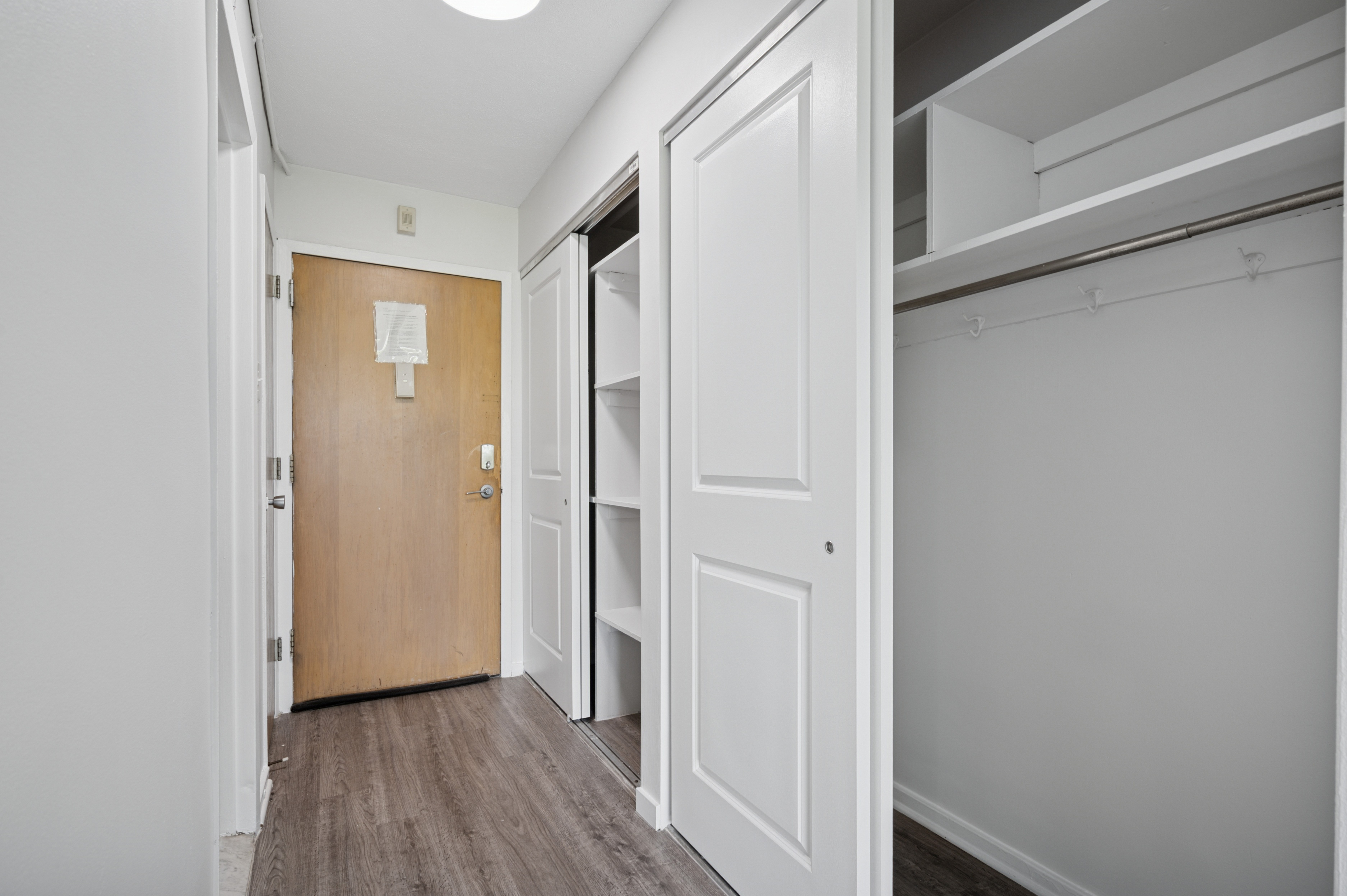 A hallway with a brown door and white walls.