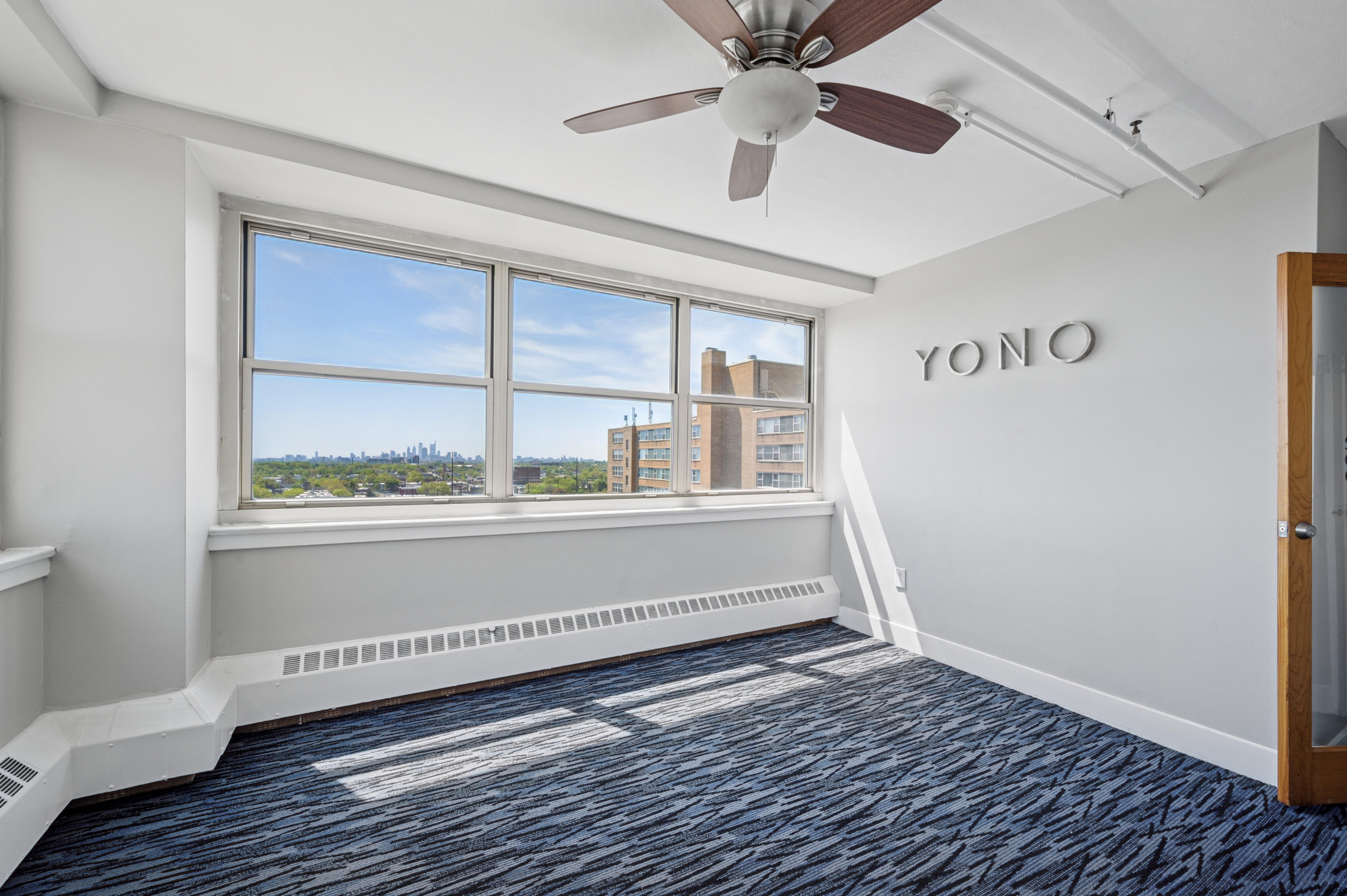 A room with a ceiling fan and a window overlooking a cityscape.