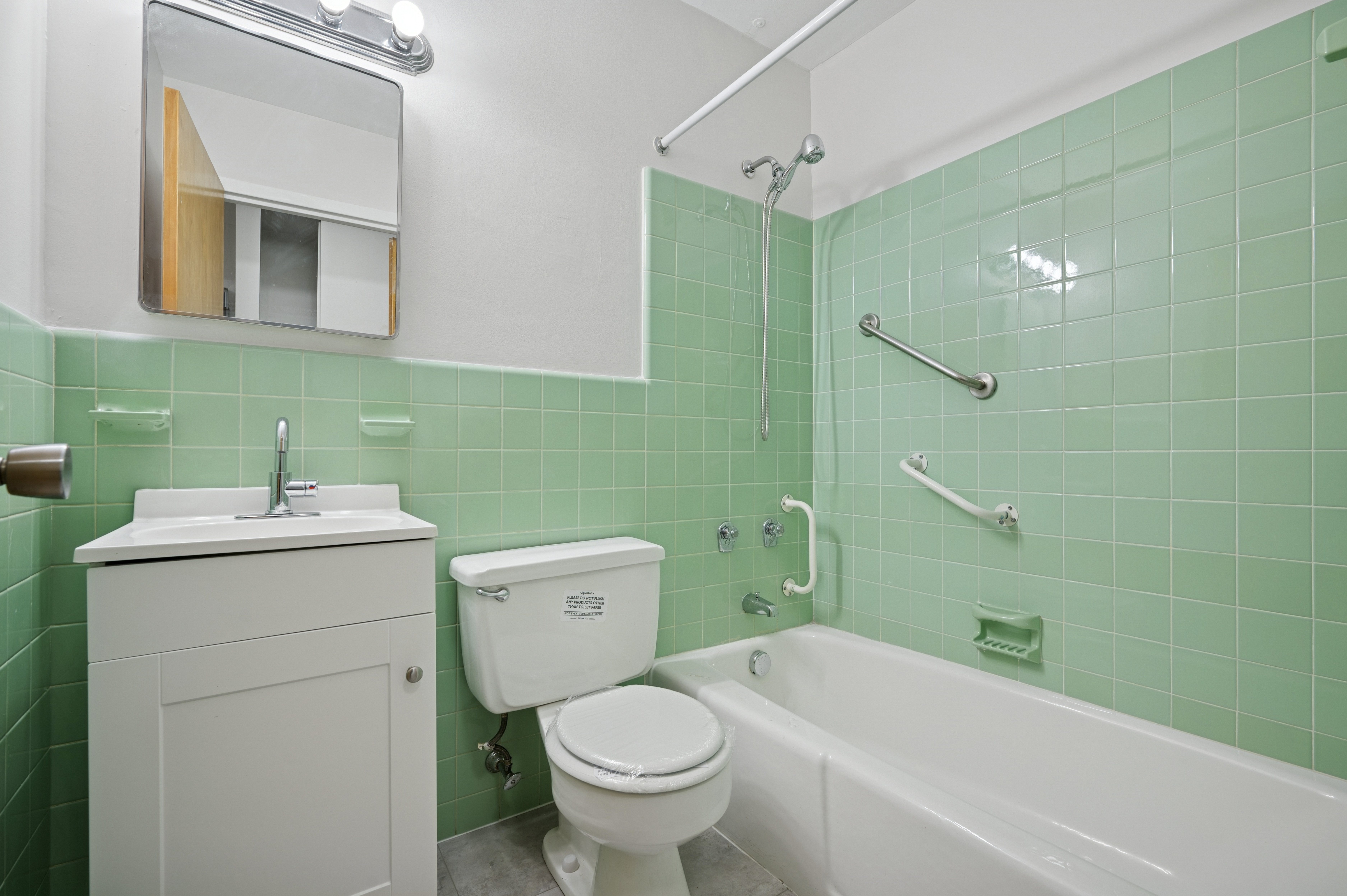 A white toilet sits next to a bathtub in a green tiled bathroom.