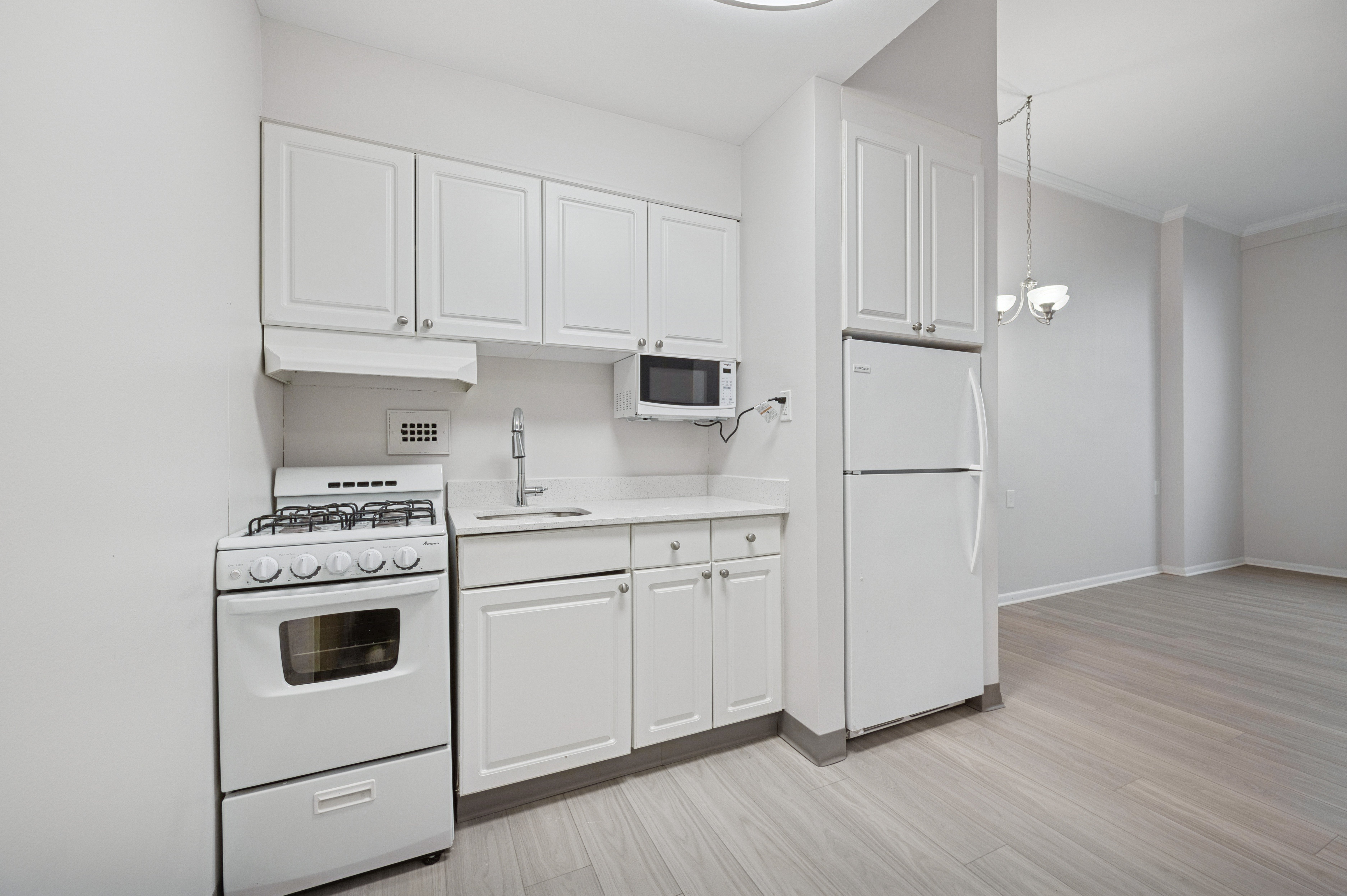 A white kitchen with a refrigerator, microwave, oven, and sink.