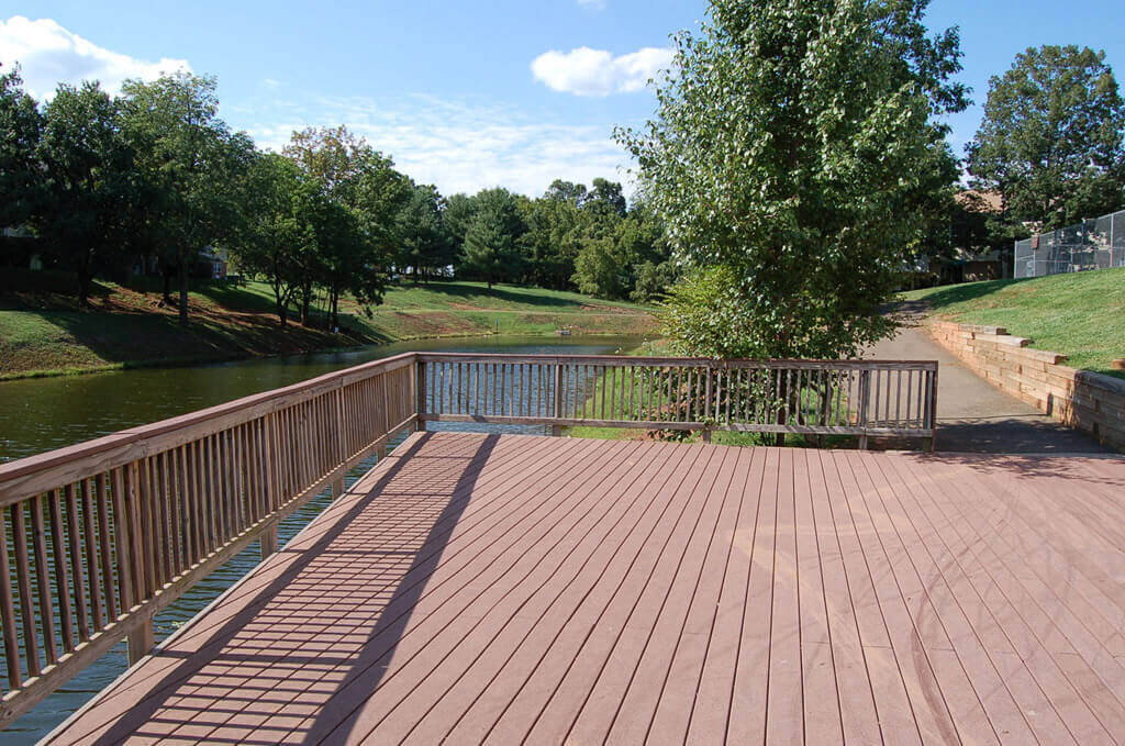 A large wood deck with a railing overlooking lush landscaping and a pond at the Brentwood Apartment Homes in Manassas, Virginia.