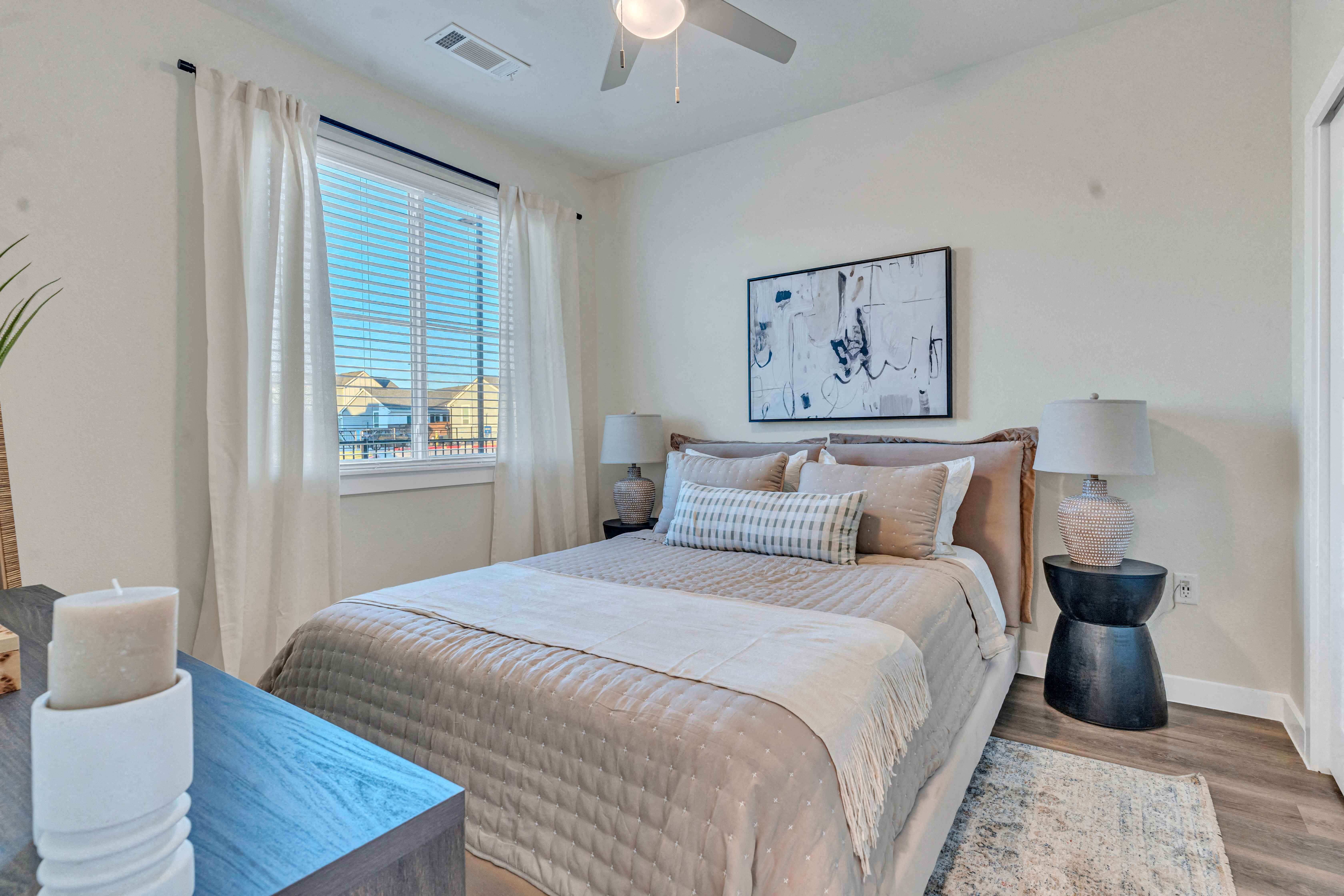 A bedroom with a large bed, a ceiling fan, and a painting on the wall.