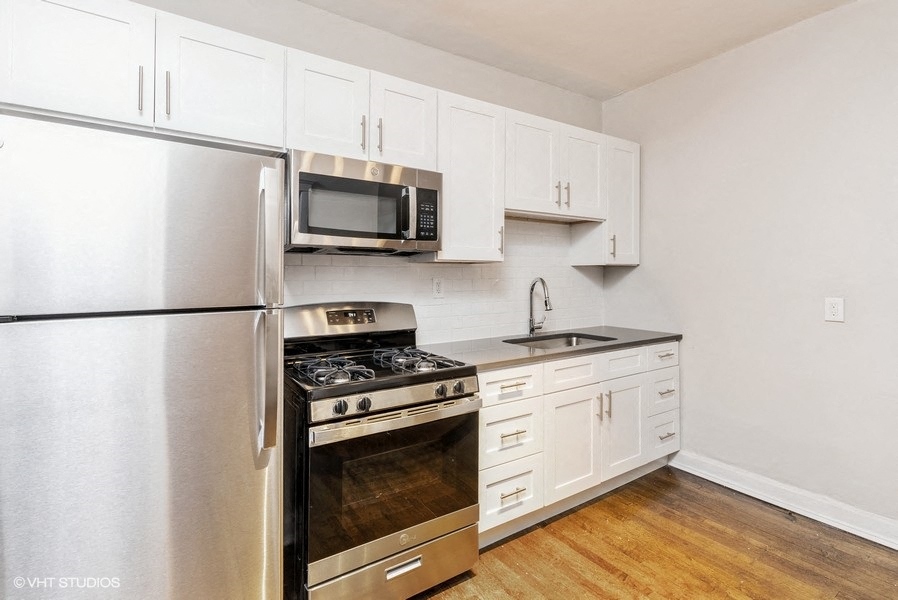 Renovated kitchen with white cabinets, stone countertops, and stainless steel appliances  at Ivy Promenade | Hyde Park Chicago Apartments near UChicago | 5447 S Woodlawn Ave